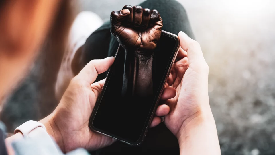 En mørkhudet hånd med knyttet neve kommer ut av en mobiltelefon
